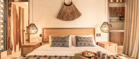 A neatly arranged bedroom with a large bed, bedside tables, a bedside lamp, a decorative wall hanging, and a tray with food and drinks on the bed.