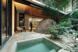 A modern interior with a glass door, a seating area with chairs, a small pool, and tropical plants.