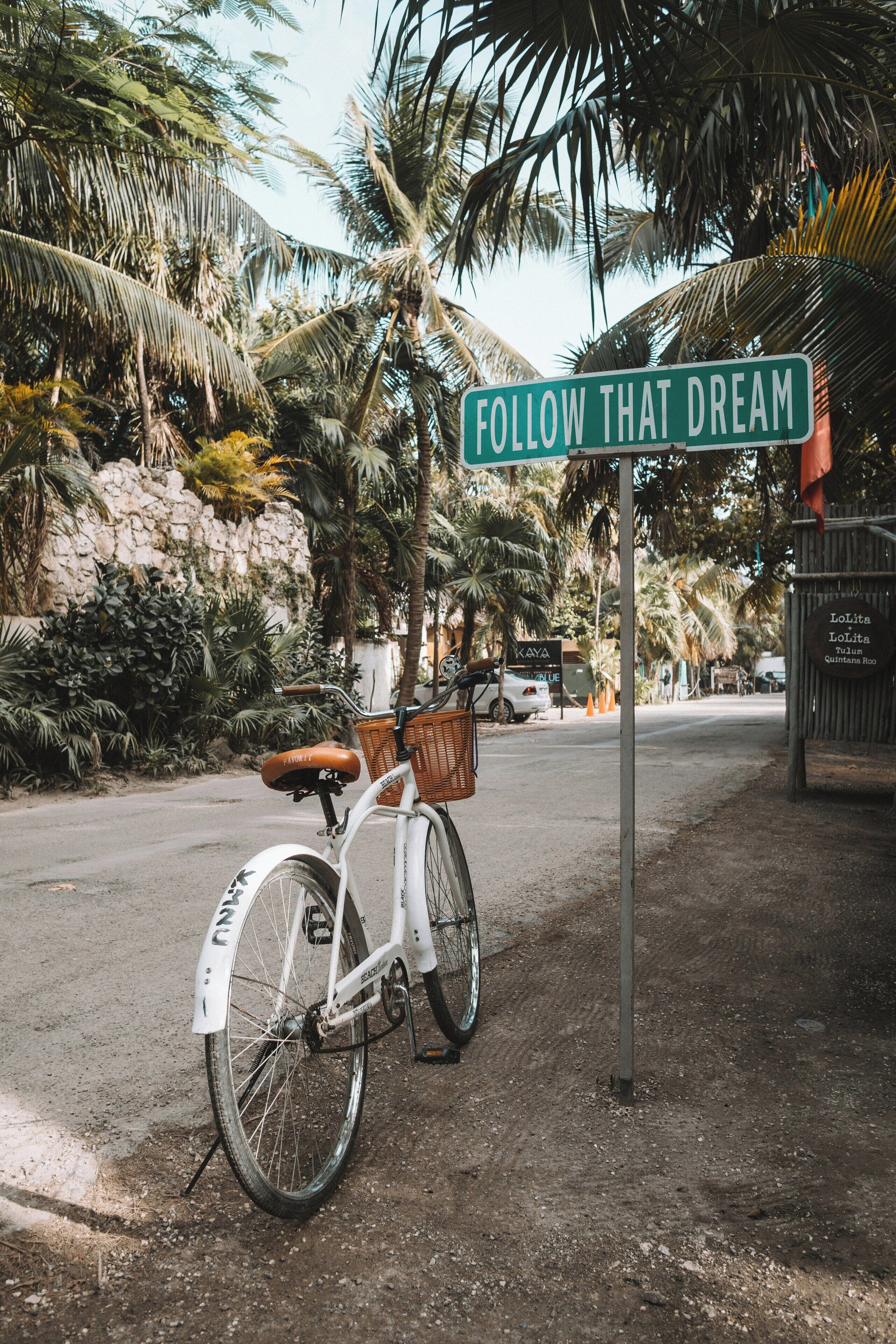 Un vélo garé sur un chemin de terre, avec un panneau indiquant : « SUIVEZ VOS RÊVES ».
