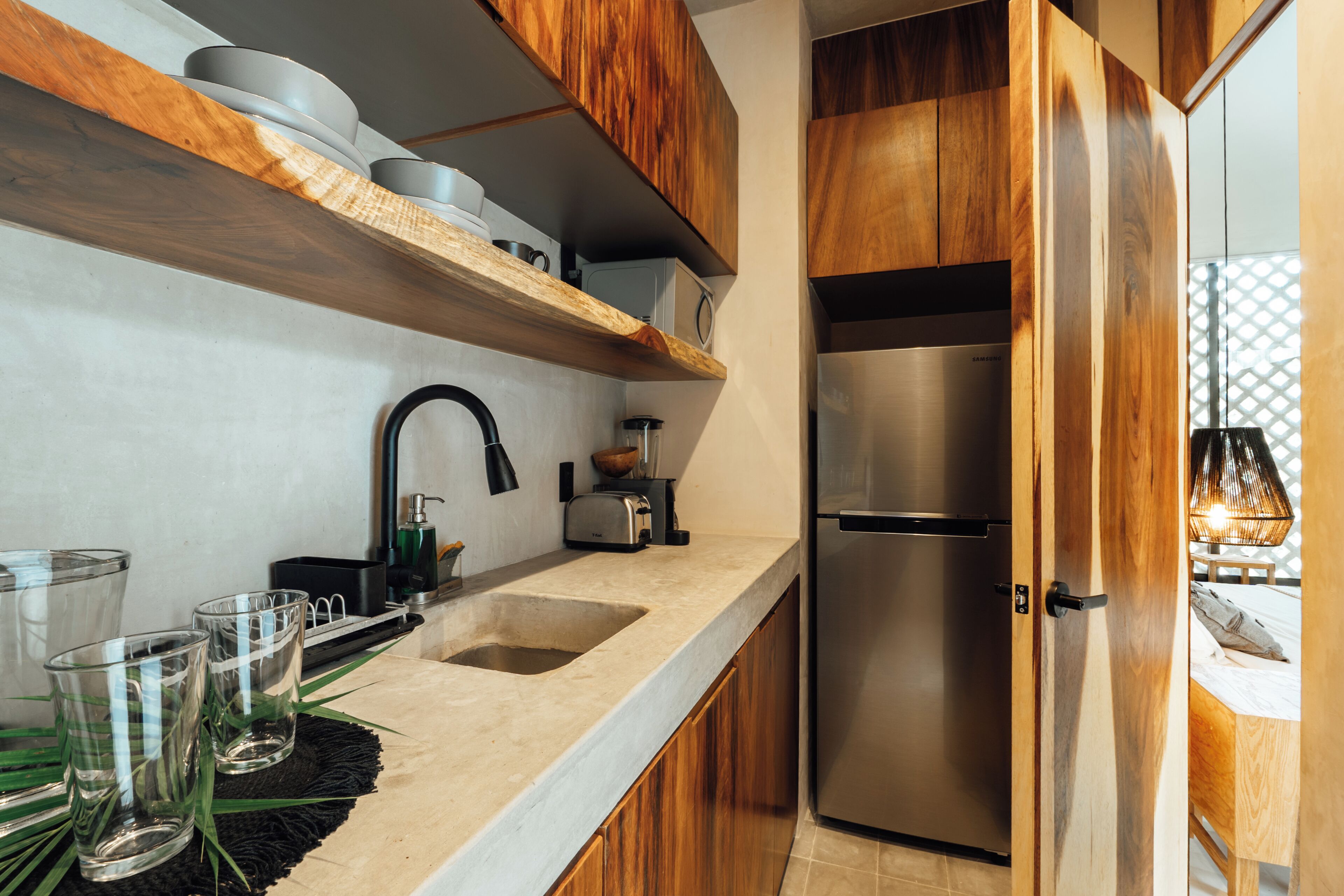 A modern kitchen with wooden cabinets, a stainless steel refrigerator, a built-in oven, and a countertop with glassware and a coffee maker.