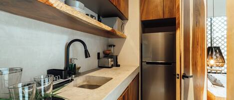 A modern kitchen with wooden cabinets, a stainless steel refrigerator, a built-in oven, and a countertop with glassware and a coffee maker.