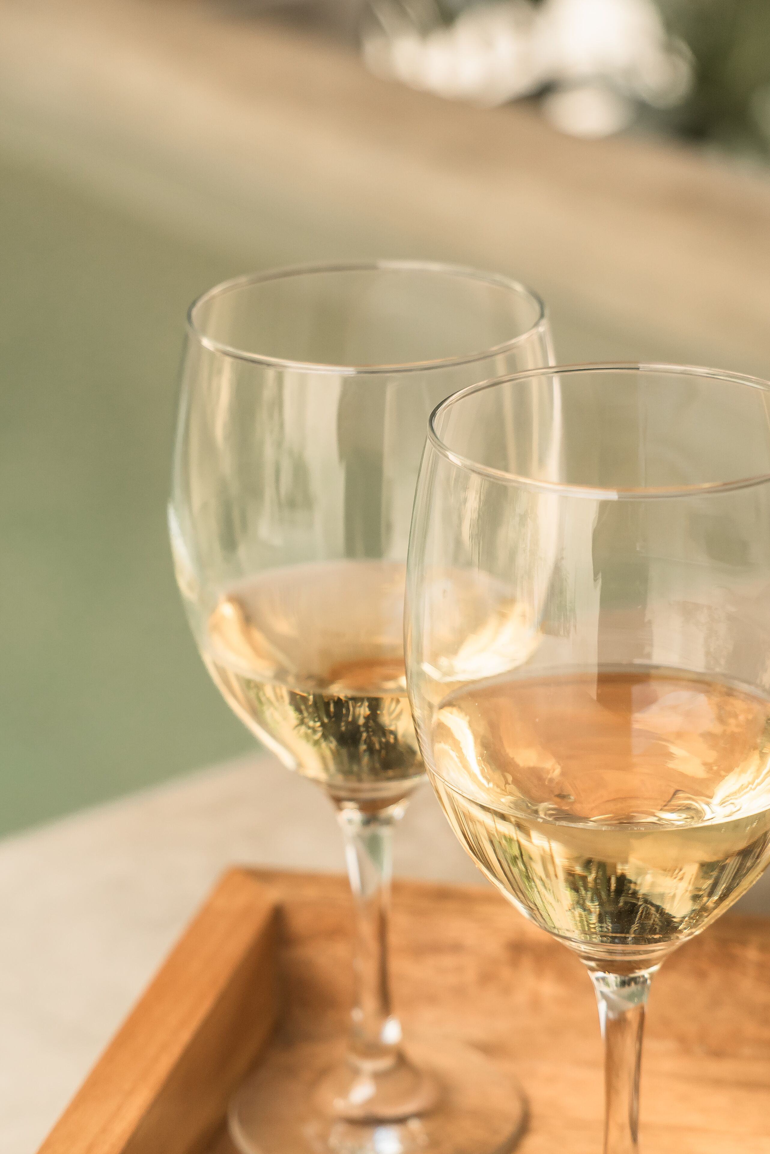Two wine glasses on a wooden tray.