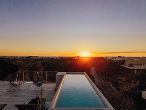 Una piscina en la azotea con vistas a la puesta de sol sobre un paisaje urbano.