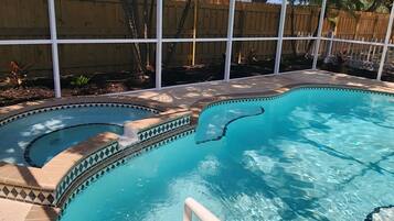 Une piscine au design incurvé, entourée d’une clôture en bois et de palmiers.