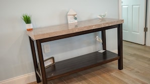 A dark wooden console table with a light-colored top, a small potted plant, a decorative house-shaped sign, and a glass ornament. - Newly Renovated Family Vacation Rental with Pool & Spa (Bradenton)
