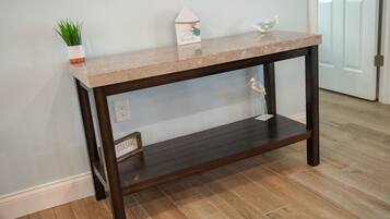 Une console en bois foncé, surmontée d’un plateau de couleur claire, agrémentée d’une petite plante en pot, d’un panneau décoratif en forme de maison et d’un ornement en verre.
