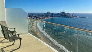 A balcony with a chair, offering a view of a coastal cityscape with buildings and a beach. - Condos SVLC (Mazatlán)