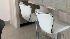 A modern kitchen with a granite countertop, stainless steel sink, and two white bar stools. - Condos SVLC (Mazatlán)