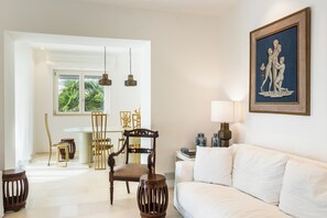 Una habitación bien iluminada con un sofá blanco, una mesa de comedor con sillas y una obra de arte enmarcada en la pared.