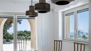 A dining area with a table set for four, large windows with a view of the sea, and a ceiling with a unique design.