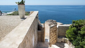 A coastal property with a concrete balcony overlooking the sea, a potted plant, and a stone wall.