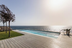 Una piscina con vista al océano, una terraza de madera y algunos árboles.