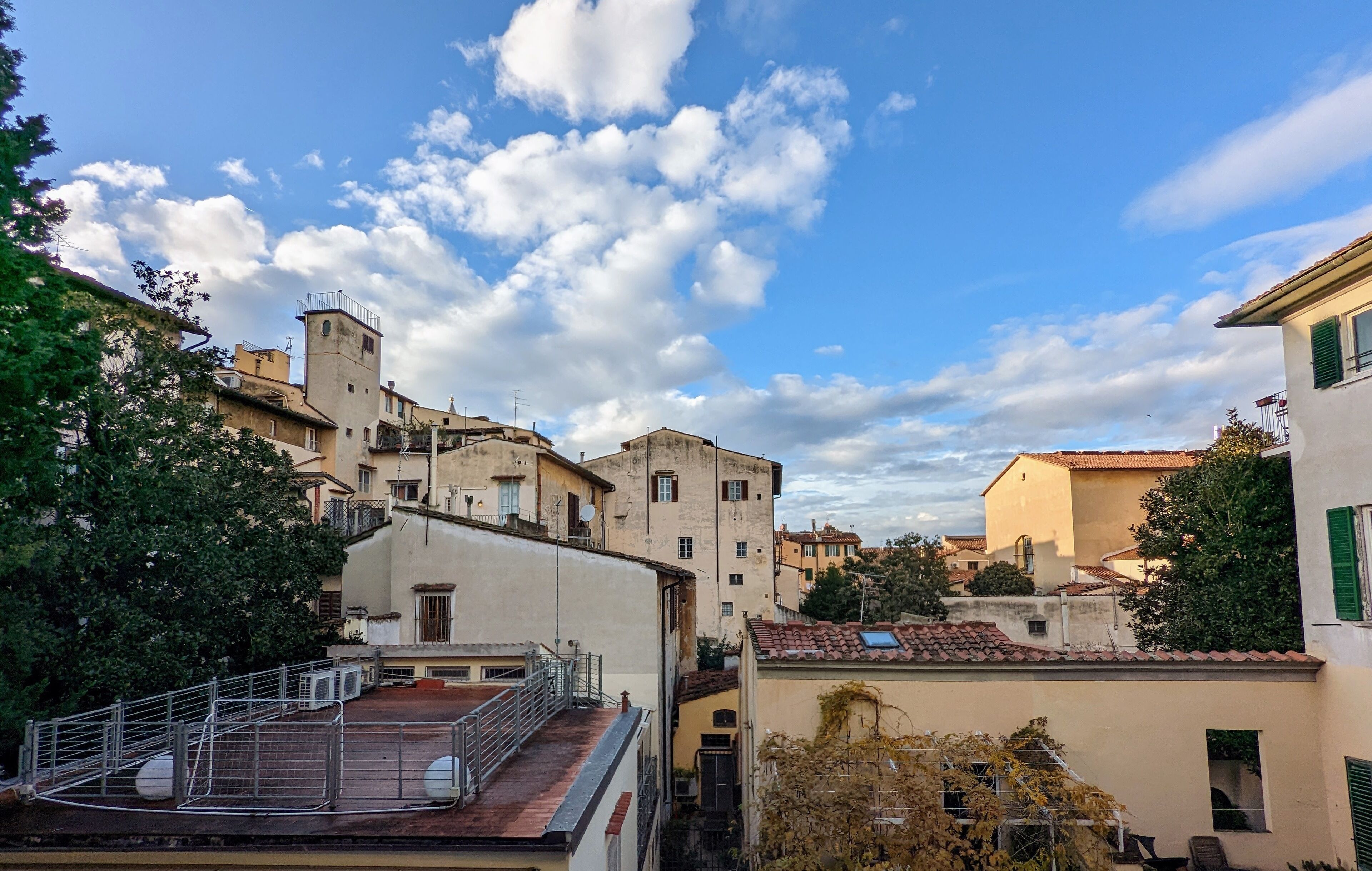 A traditional Mediterranean town with terracotta-roofed buildings, a prominent tower, and a clear blue sky with scattered clouds.