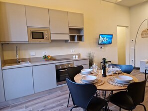 Una cocina moderna con microondas, horno y lavaplatos. Hay una mesa de comedor preparada con platos, vasos y una botella. Un televisor está montado en la pared.