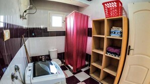 A bathroom with a white bathtub, a red shower curtain, and a wooden shelf unit with folded towels. - Cozy Rooftop LS #6 (Safaga)