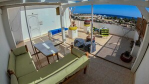 A rooftop terrace with a green sofa, a small table, and a view of the sea and buildings. - Cozy Rooftop LS #6 (Safaga)