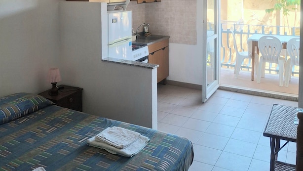 A bedroom with a bed, a nightstand, a ceiling fan, and a kitchenette with cabinets and a refrigerator. - Marina, seaside area, 5 min.walk beach, 15 min. trainstation, wi fi. parking. (Tropea)