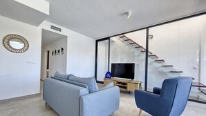 Ein modernes Wohnzimmer mit einer Couch, einem blauen Sessel und einem Fernseher auf einem Holzboden.