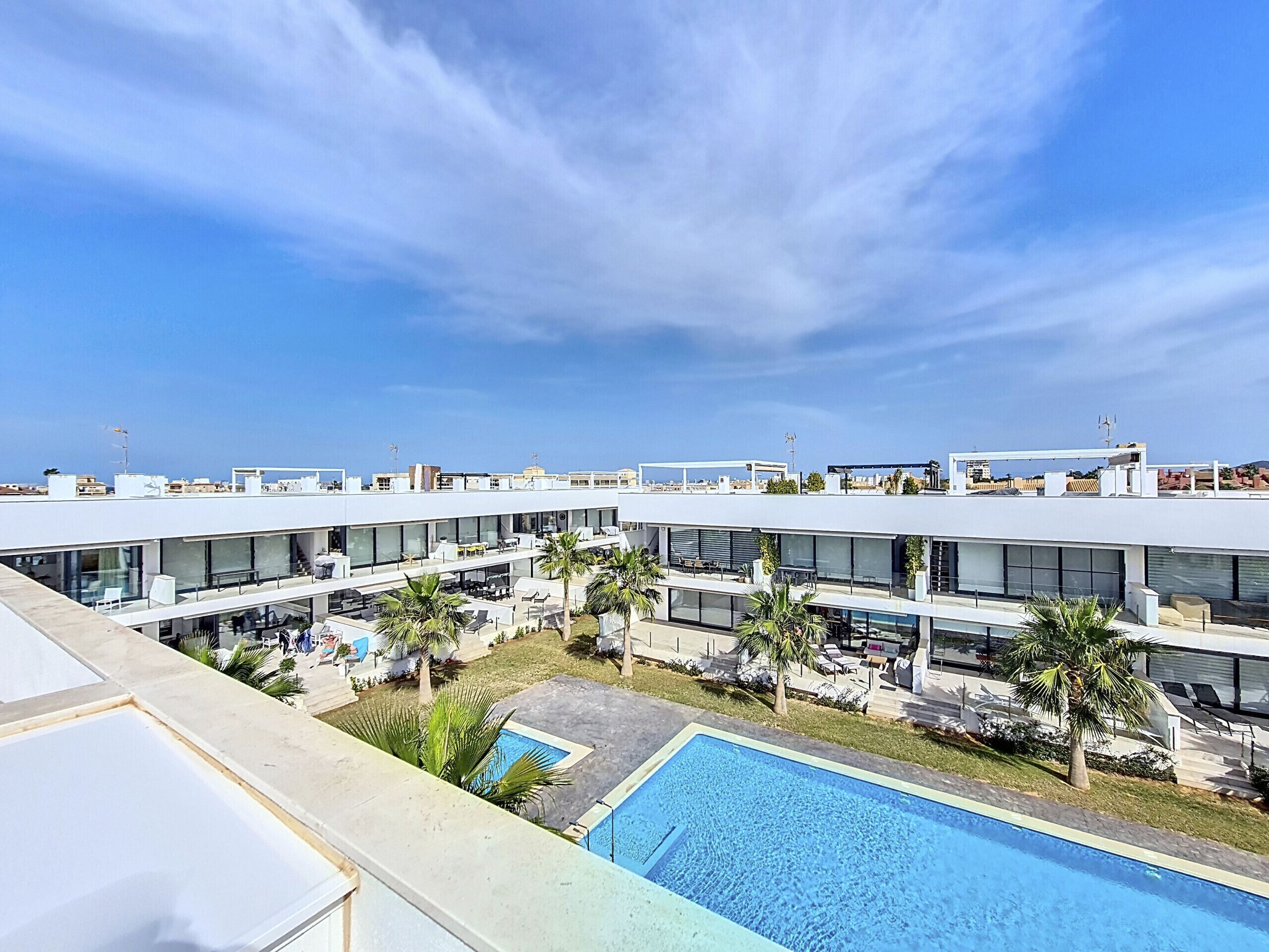 Et moderne hotel med flere etager, udendørs siddeområder og en swimmingpool.
