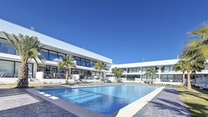 Ein modernes Gebäude mit Swimmingpool, Palmen und einem sechseckigen Steinweg.