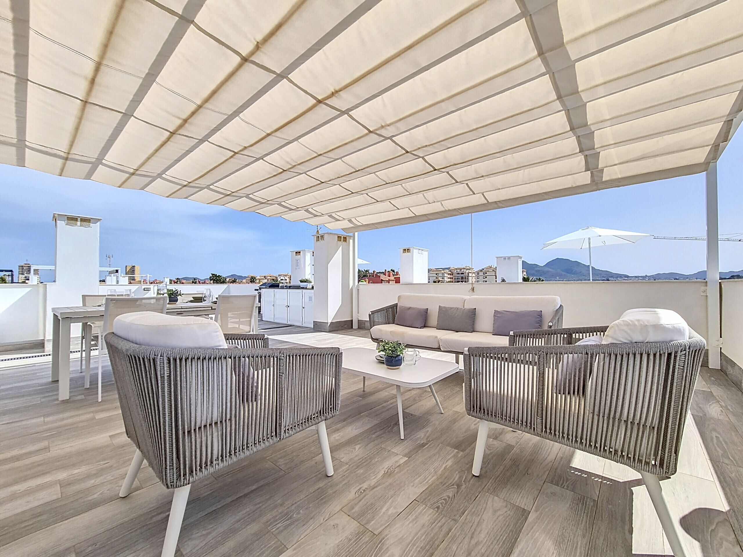 Terraza en la azotea con mobiliario de mimbre, una mesa de comedor y un sofá.