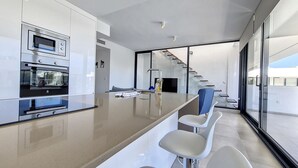 Eine moderne Küche mit integrierten Geräten, einer zentralen Kochinsel mit Barhocker und einer Treppe zu einer oberen Ebene.