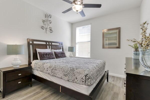 A bedroom with a bed, nightstands, a ceiling fan, a window, and a framed picture on the wall.