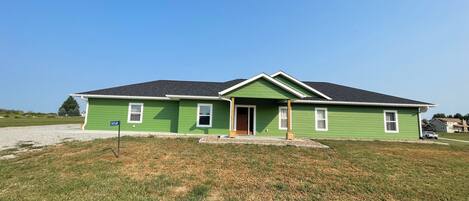 A green single-story house with a front porch, a driveway, and a grassy yard.