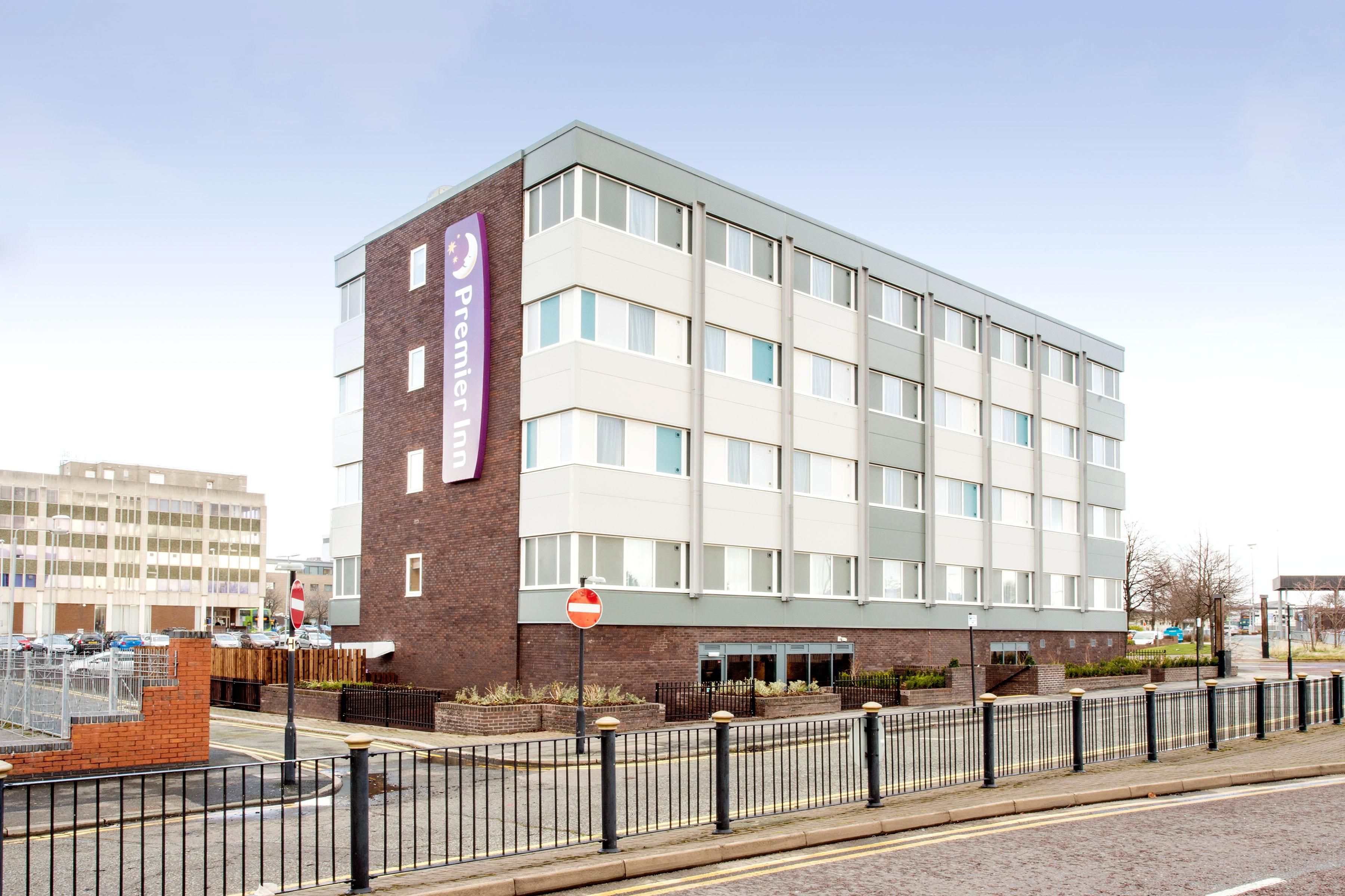 Et hotel over flere etager med et tydeligt 'Premier Inn' skilt, en murstensfacade og et moderne design.