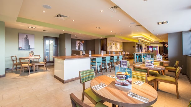 A modern restaurant with round tables, bar seating, and a view of the cityscape. - Premier Inn Birkenhead Town Centre (Birkenhead)
