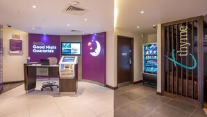 A reception desk with a 'Check In' sign, a 'Good Night Guarantee' sign, a vending machine, and a 'Thyme' sign. - Premier Inn Birkenhead Town Centre (Birkenhead)