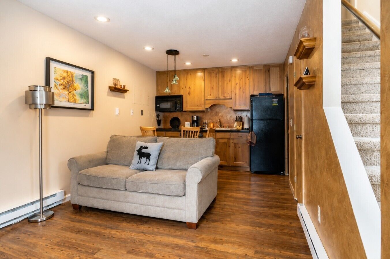 Ein Wohnzimmer mit einer Couch, einem Esstisch und einer Küchenzeile mit Holzschränken und einem schwarzen Kühlschrank.