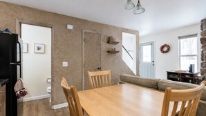 A dining area with a wooden table and chairs, a black refrigerator, and a stone wall.