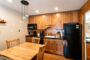 A compact kitchen with wooden cabinets, a black refrigerator, a microwave, and a dining table with chairs.