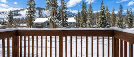 Une terrasse en bois recouverte de neige, entourée d’arbres chargés de neige et avec une montagne en toile de fond.