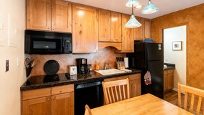 A compact kitchen with wooden cabinets, a black microwave, a coffee maker, and a black refrigerator.