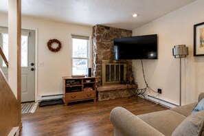 A living room with a stone fireplace, a flat-screen TV mounted on the wall, a wooden entertainment unit, and a couch.