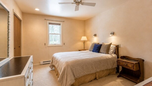 A bedroom with a bed, bedside table, lamp, window, and ceiling fan.