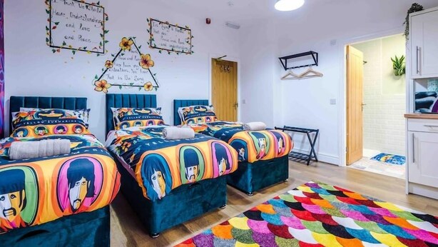 A room with three beds, each with colorful bedding featuring cartoon characters. There are wall decorations with inspirational quotes and a small table with a plant. - Beatles Themed Hotel (Liverpool)