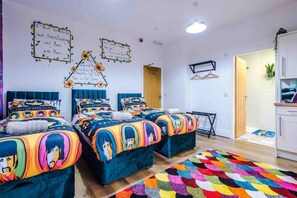 A room with three beds, each with colorful bedding featuring cartoon characters. There are wall decorations with inspirational quotes and a small table with a plant. - Beatles Themed Hotel (Liverpool)