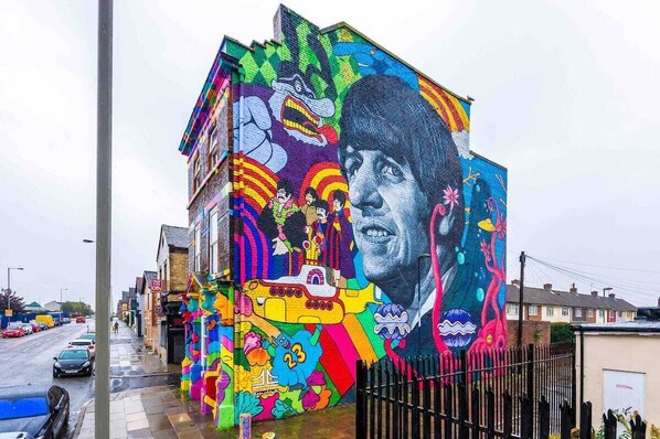 A colorful mural on a building with a large portrait and various abstract designs. - Beatles Themed Hotel (Liverpool)