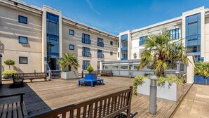 Um terraço moderno ao ar livre com piso de madeira, assentos azuis e plantas em vasos.