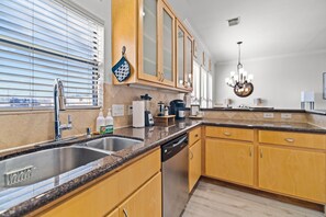 A modern kitchen with granite countertops, stainless steel appliances, wooden cabinets, and a chandelier.