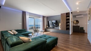Una sala de estar moderna con un sofá seccional verde, un televisor de pantalla plana y un comedor con una mesa pequeña y sillas.
