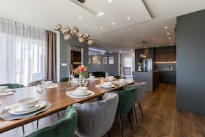Un espace repas moderne avec une table en bois dressée pour six personnes, entourée de chaises à l’assise rembourrée de tissu vert.