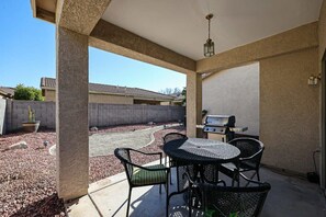 An outdoor patio with a round table and chairs, a grill, and a view of a residential area.