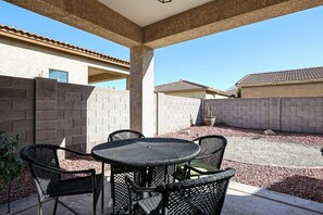 A covered patio area with a round table and four chairs, surrounded by a low brick wall and a gravel ground.