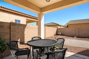 A covered patio area with a round table and four chairs, surrounded by a low brick wall and a clear blue sky. - Pet-Friendly 3BR | Fenced Yard | King Bed (Chandler)