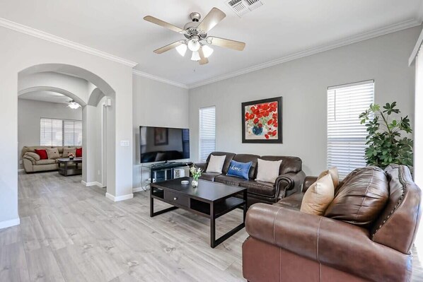 A modern living room with a dark coffee table, leather sofas, a flat-screen TV, and a ceiling fan.