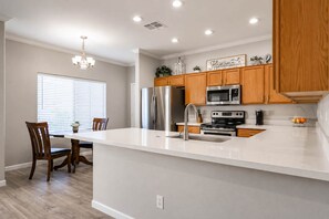 A modern kitchen with a central island, stainless steel appliances, wooden cabinets, and a chandelier. - Pet-Friendly 3BR | Fenced Yard | King Bed (Chandler)